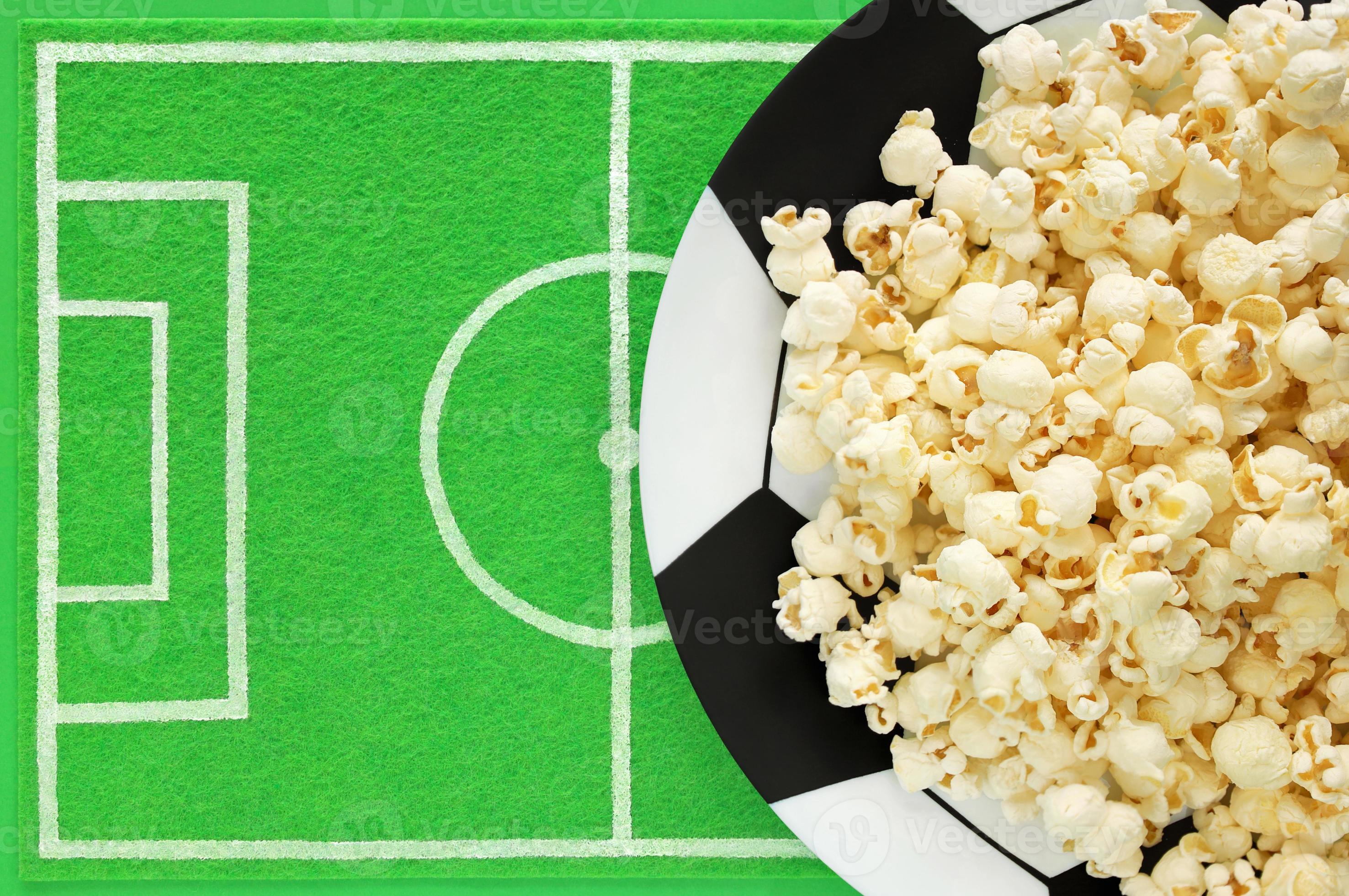 pop-corn sur une grande assiette peinte comme un ballon de football et un  tapis de vaisselle comme un terrain de football en feutre vert avec place  pour le texte. modèle de table