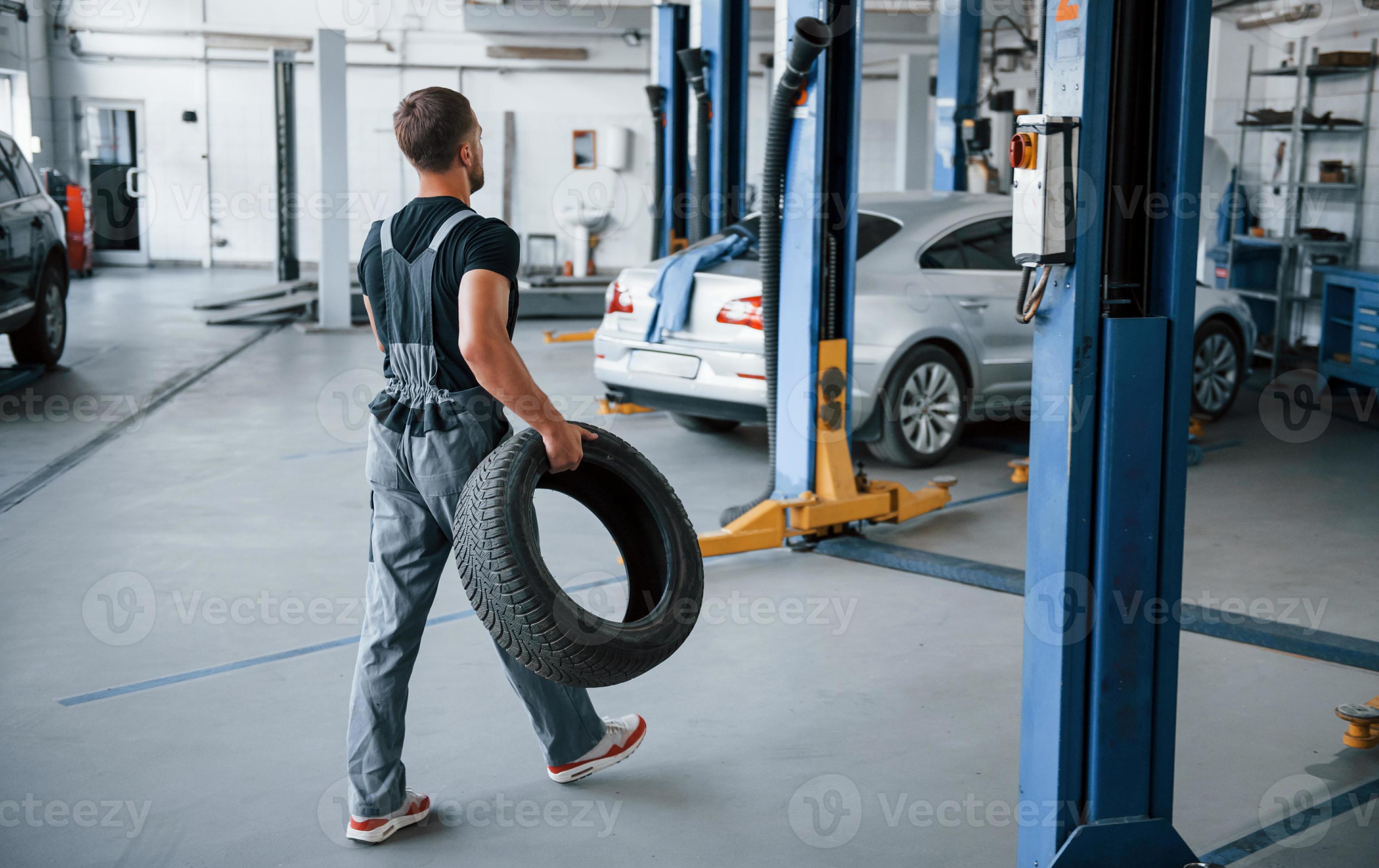 employé avec roue. le mécanicien tient un pneu au garage de