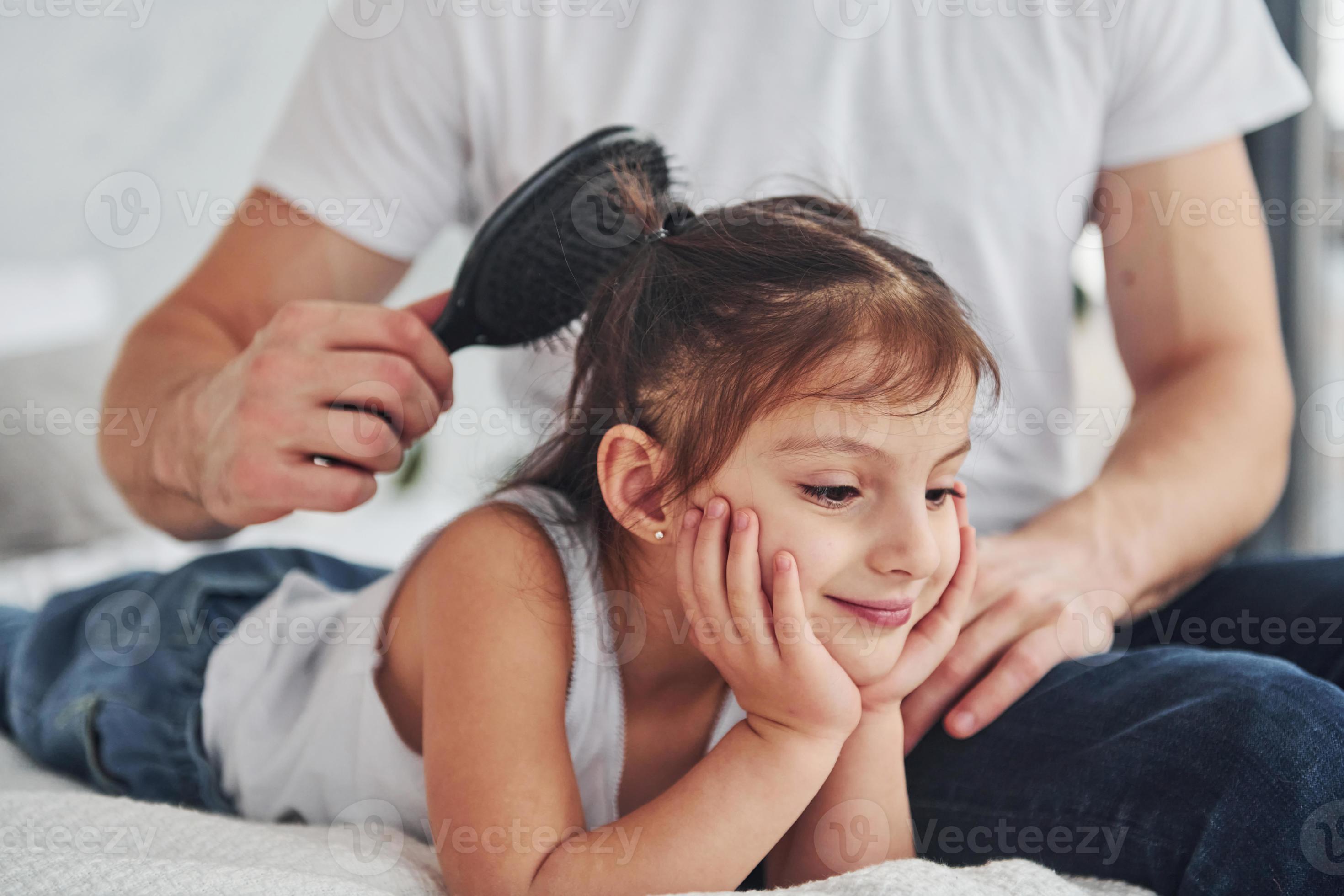 le père fait une coupe de cheveux pour sa fille en utilisant un peigne à la  maison sur le lit 15255704 Photo de stock chez Vecteezy