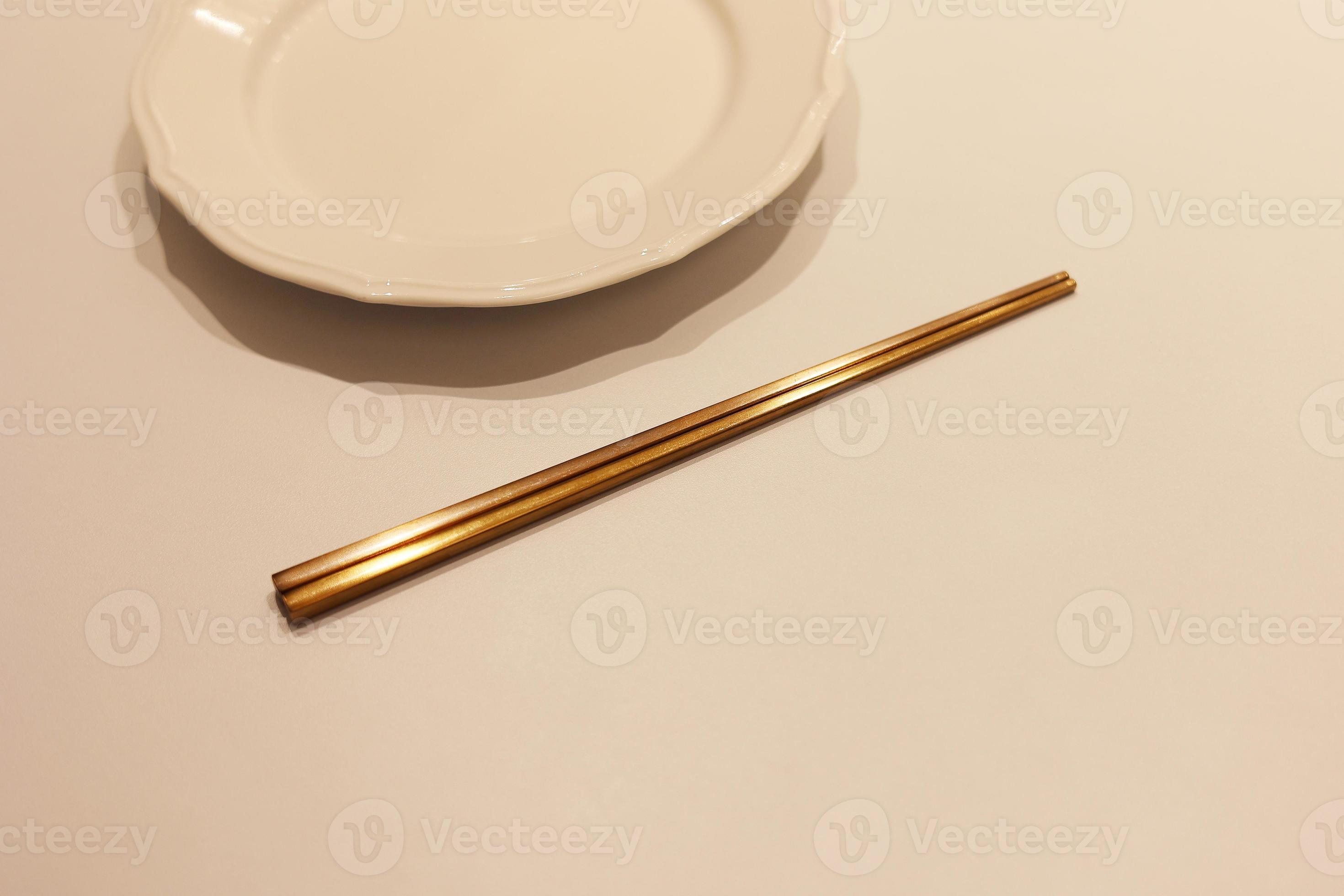 un ensemble de baguettes coréennes en laiton avec un plat blanc vide sur la  table, la baguette sur le plat 17668689 Photo de stock chez Vecteezy