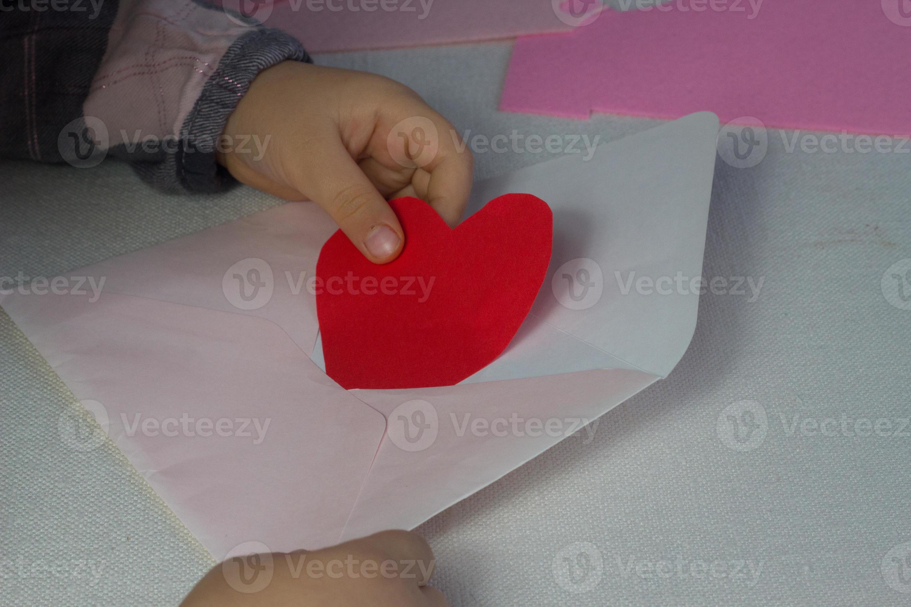 enfant tenant une lettre avec un coeur en papier rouge, une lettre