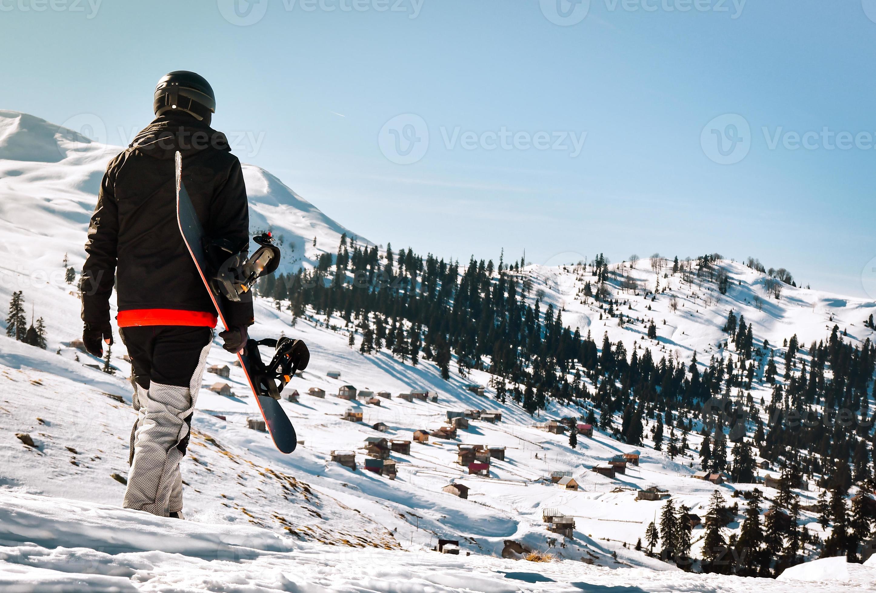 homme touriste en combinaison de ski avec snowboard dans ses mains se  promène sur une pente enneigée sur fond de magnifique paysage de montagne  19048432 Photo de stock chez Vecteezy