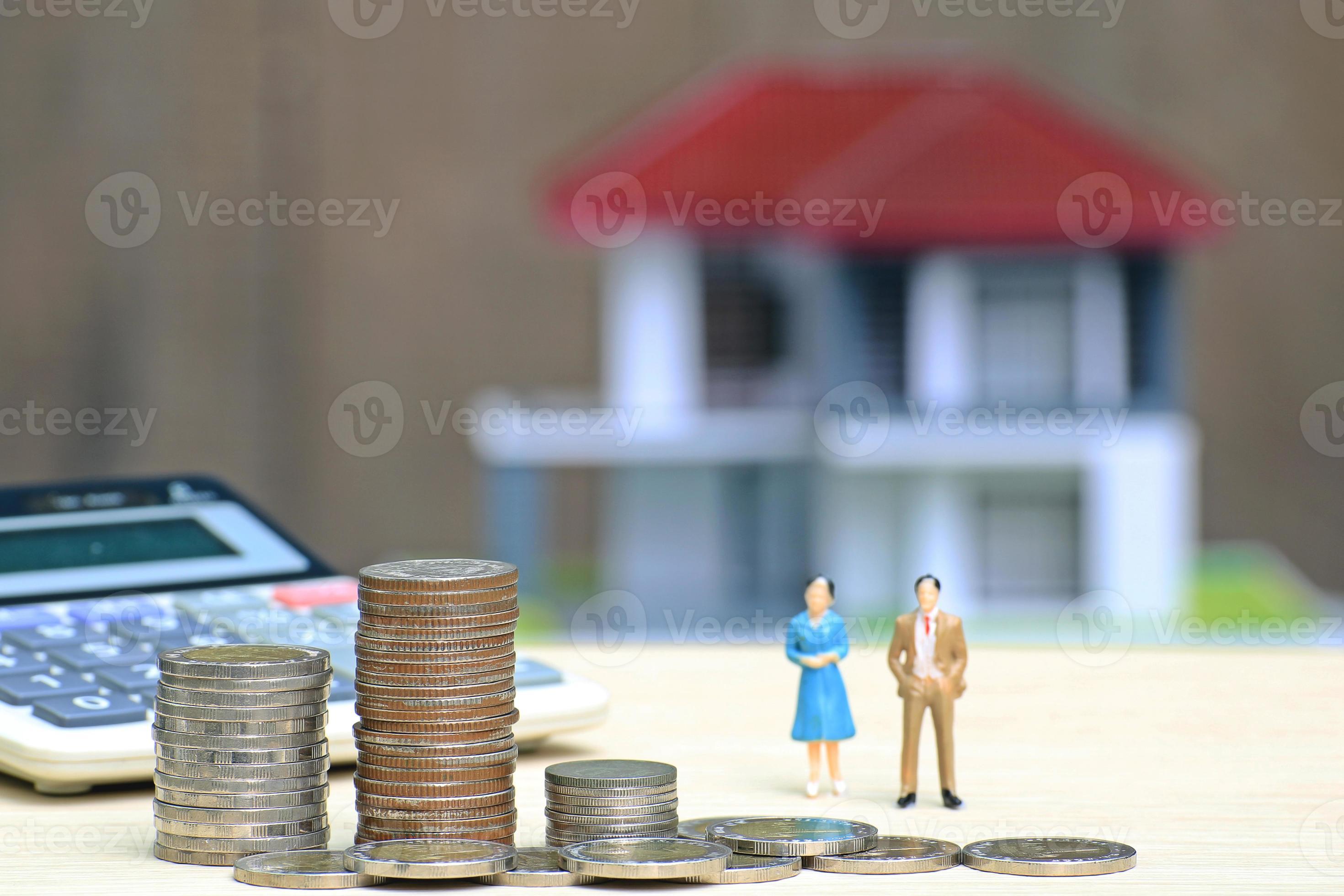 Des piles de pièces à côté de la calculatrice et des poupées miniatures homme et femme avec maison miniature en arrière-plan photo