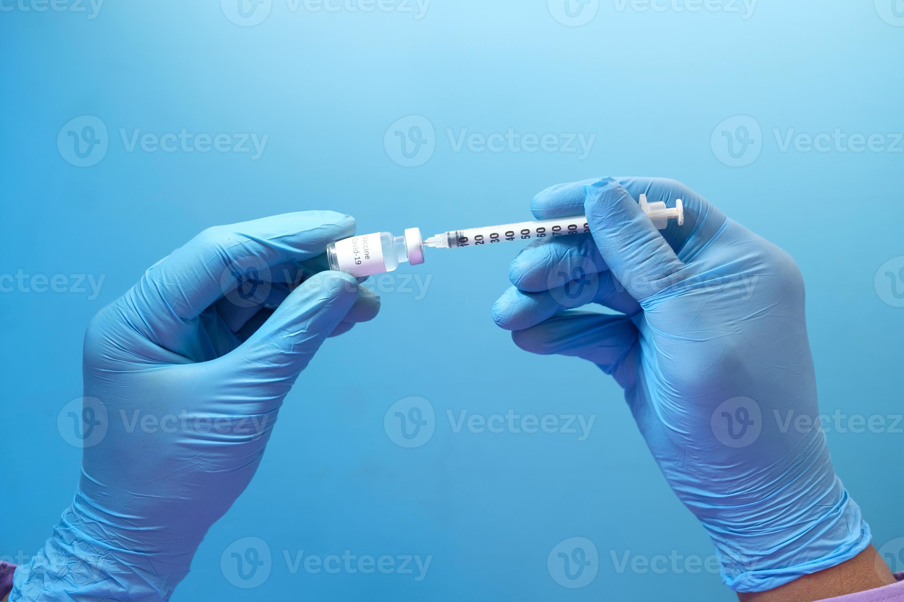 La main dans des gants en latex bleu seringue de remplissage avec des médicaments, isolé sur fond bleu photo