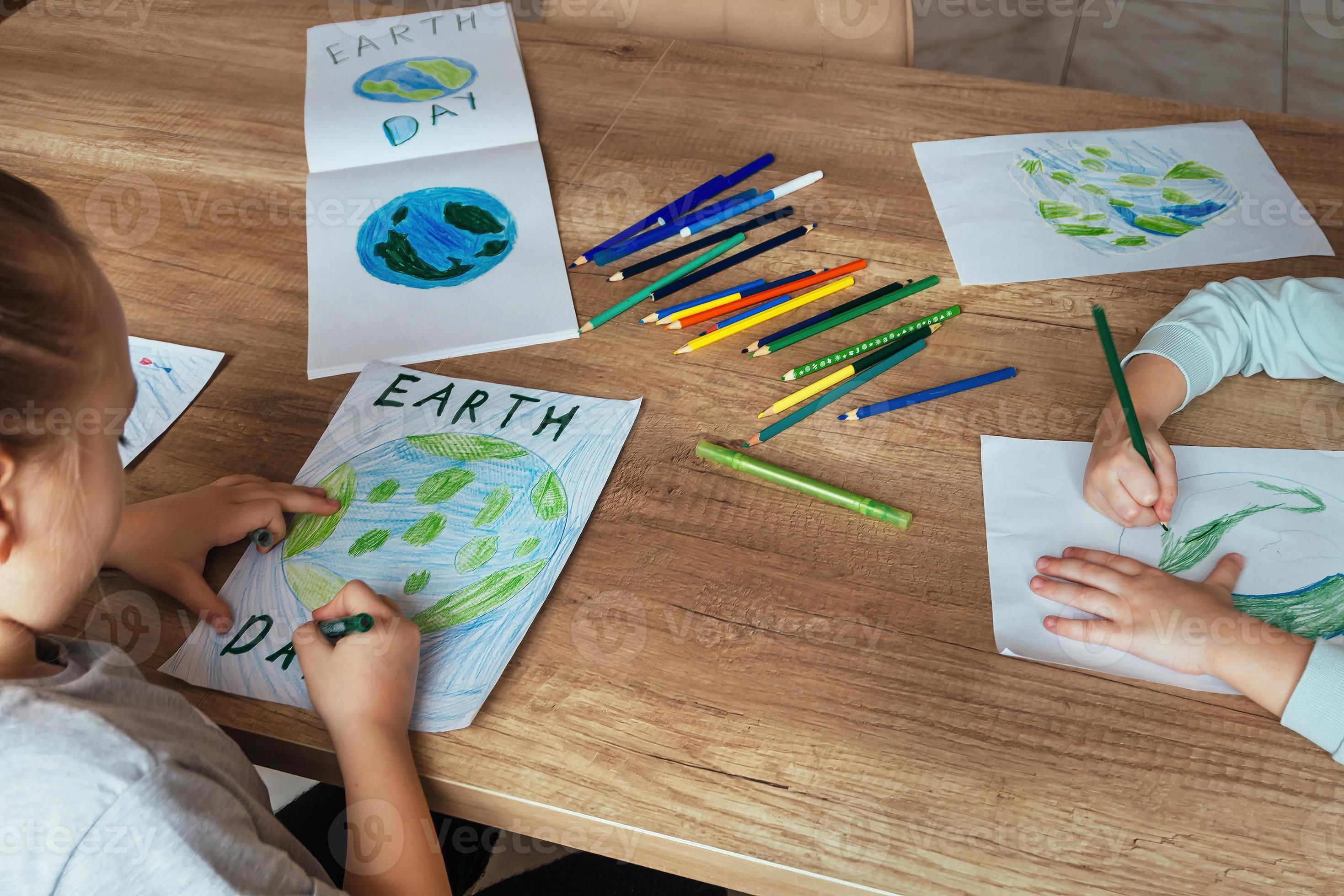 les enfants dessiner le planète Terre avec des crayons et feutre des stylos  sur album feuilles pour Terre journée à leur Accueil tableau. le concept de  protéger le environnement, paix sur Terre.