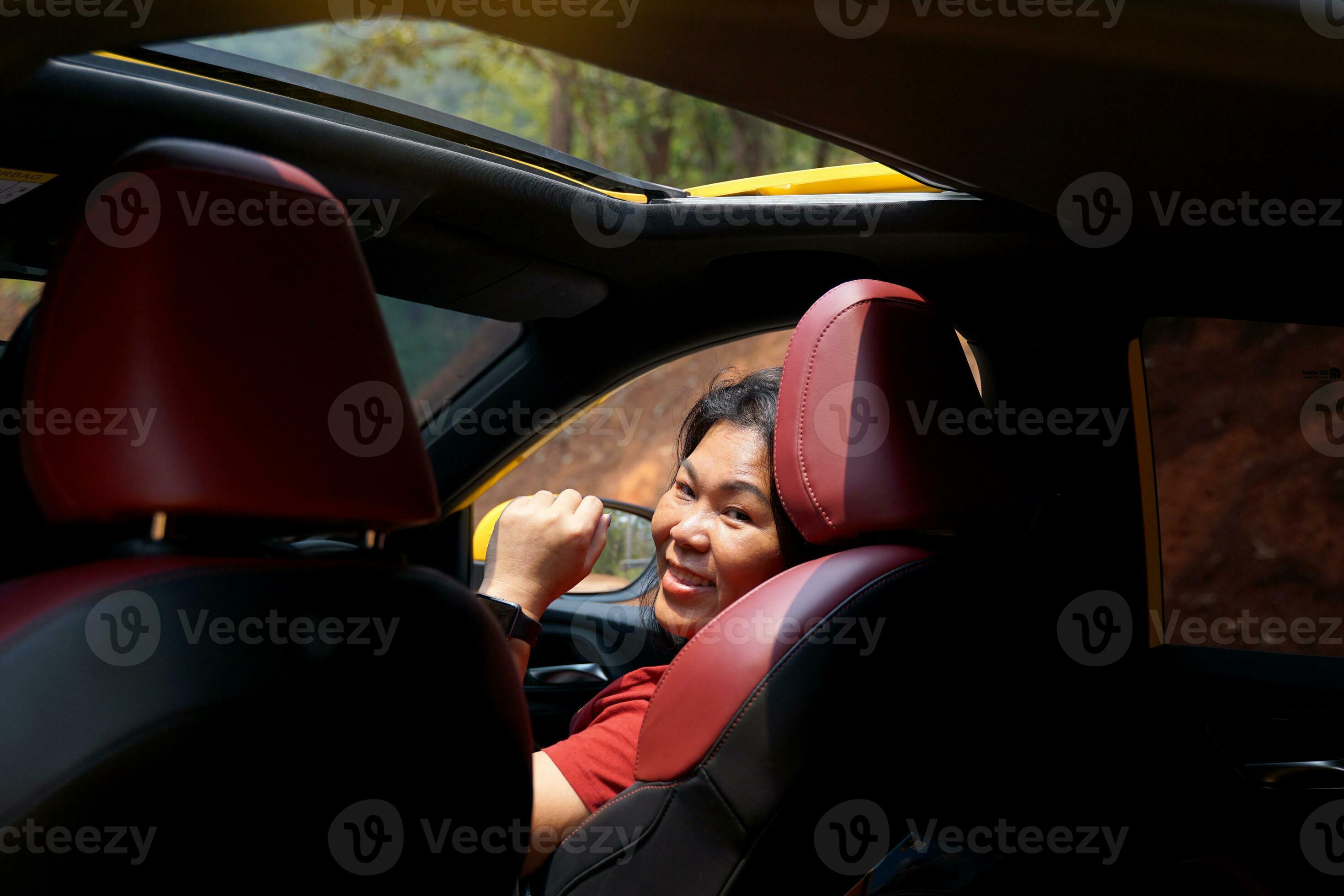 femme asiatique au volant d'une voiture jaune toit en boucle soleil ouvert  sourire heureux elle a jeté un coup d'œil derrière elle, regardant à  travers la porte arrière droite de la voiture. pendant la conduite d'un  week-end. mise au point douce et sélective