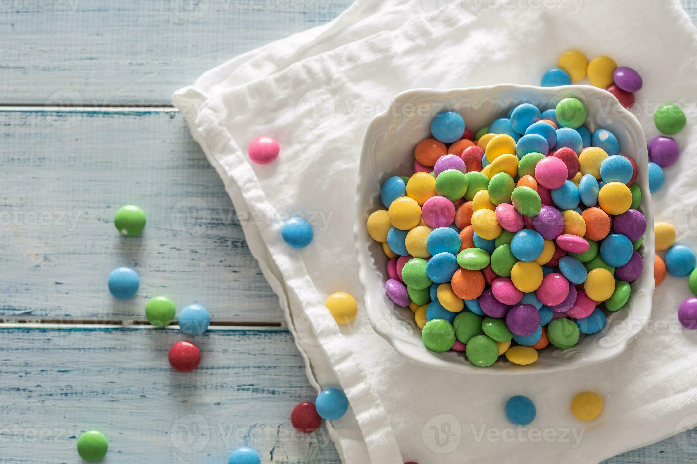 Haut vue de une bol plein de coloré bonbons sur une blanc couverture et  ancien bois avec certains épars autour 27598074 Photo de stock chez Vecteezy