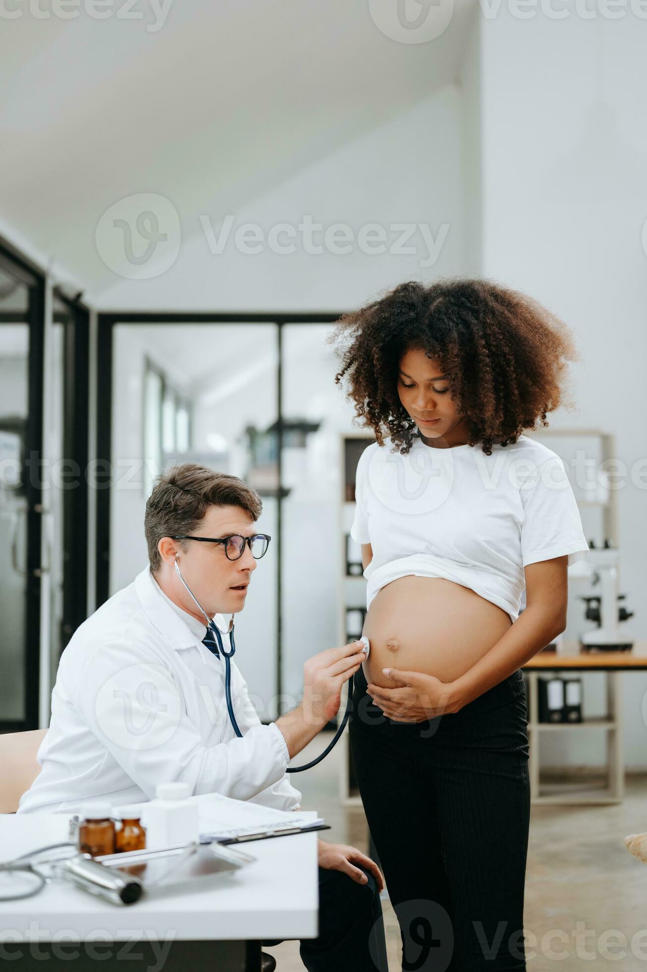 Enceinte africain femme a rendez-vous avec médecin à clinique. Masculin  gynécologue ob gynécologue médical spécialiste avec stéthoscope écoute à de  bébé battement de coeur dans de la mère ventre. grossesse, santé se