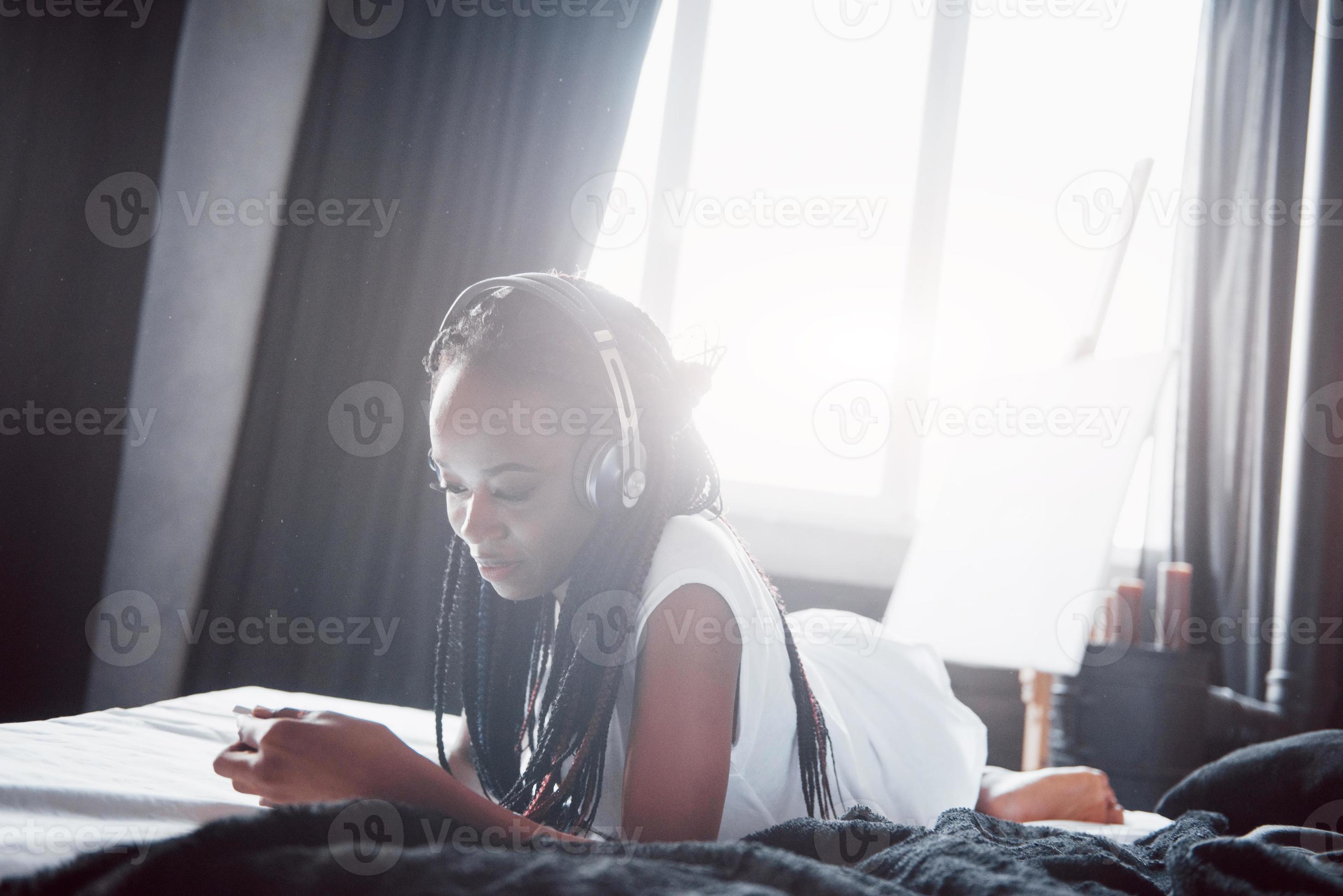 portrait d'une belle femme se réveillant dans son lit et regarde dans le  téléphone. consulter les réseaux sociaux, envoyer des sms. la fille porte  un t-shirt 3569790 Photo de stock chez Vecteezy