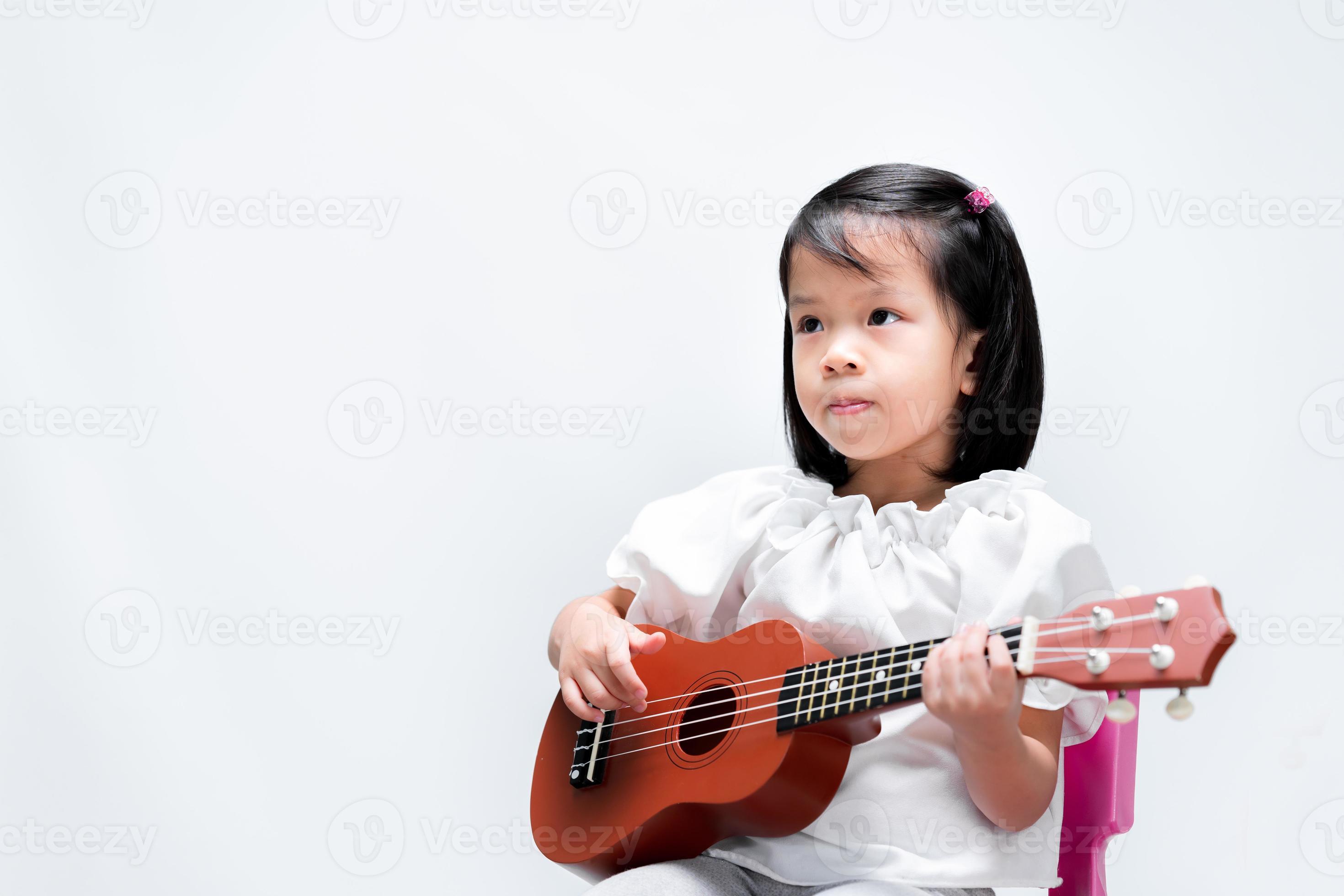 petit enfant asiatique mignon s'exerce à jouer du ukulélé. les