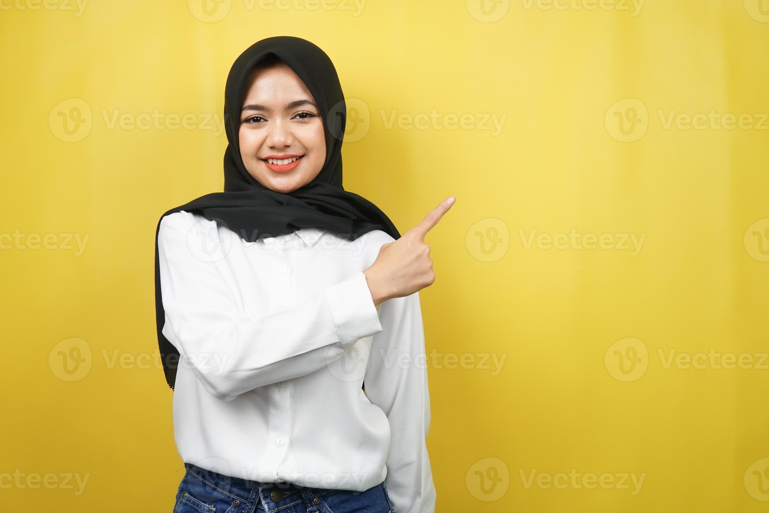 belle jeune femme musulmane asiatique avec les mains pointant l'espace vide présentant quelque chose, souriant confiant, enthousiaste, joyeux, regardant la caméra, isolé sur fond jaune photo