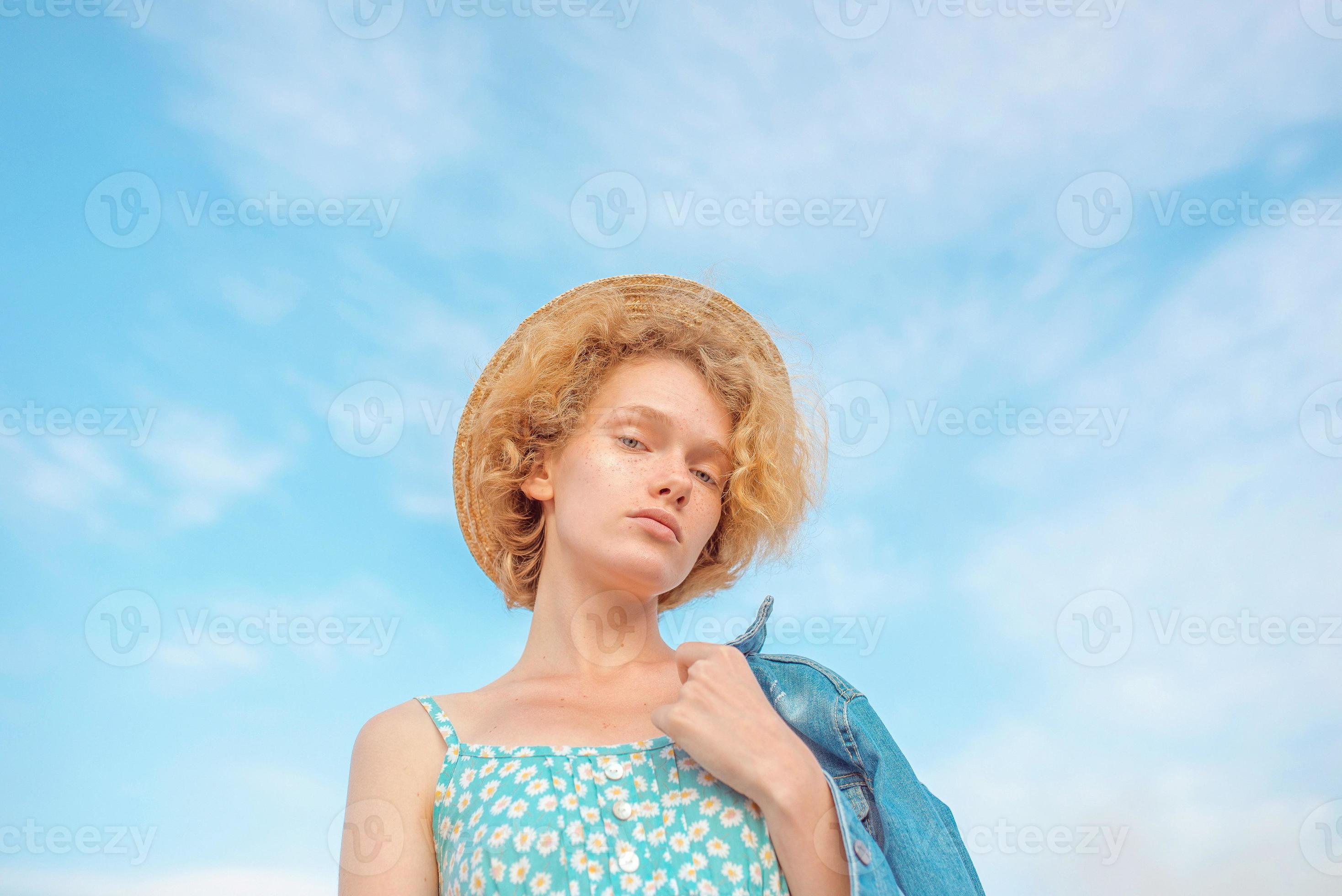 jeune femme rousse bouclée joyeuse en veste de jeans bleu tenant un chapeau  de paille dans