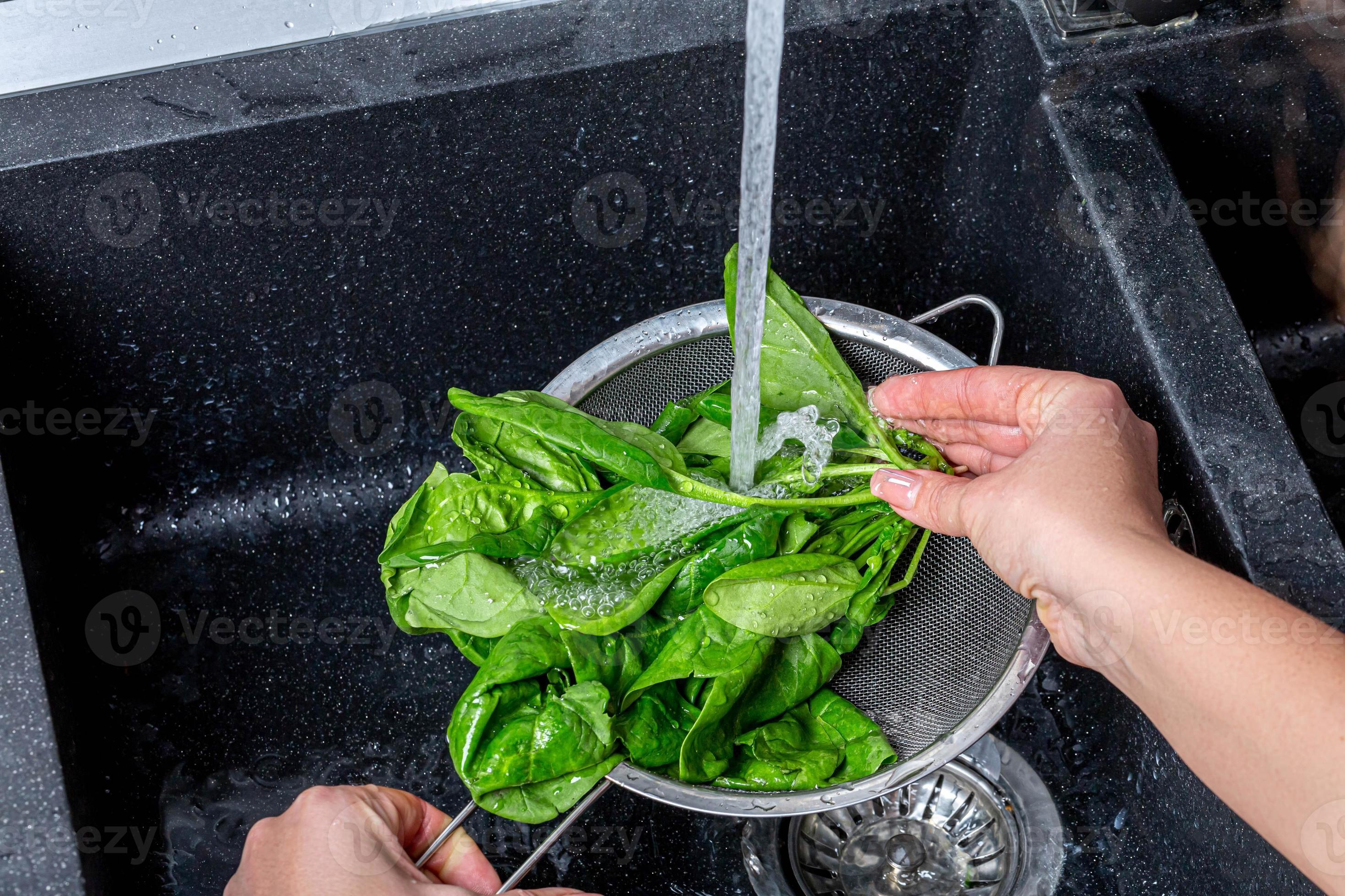 femme lave les feuilles d'épinards frais sous l'eau courante photo