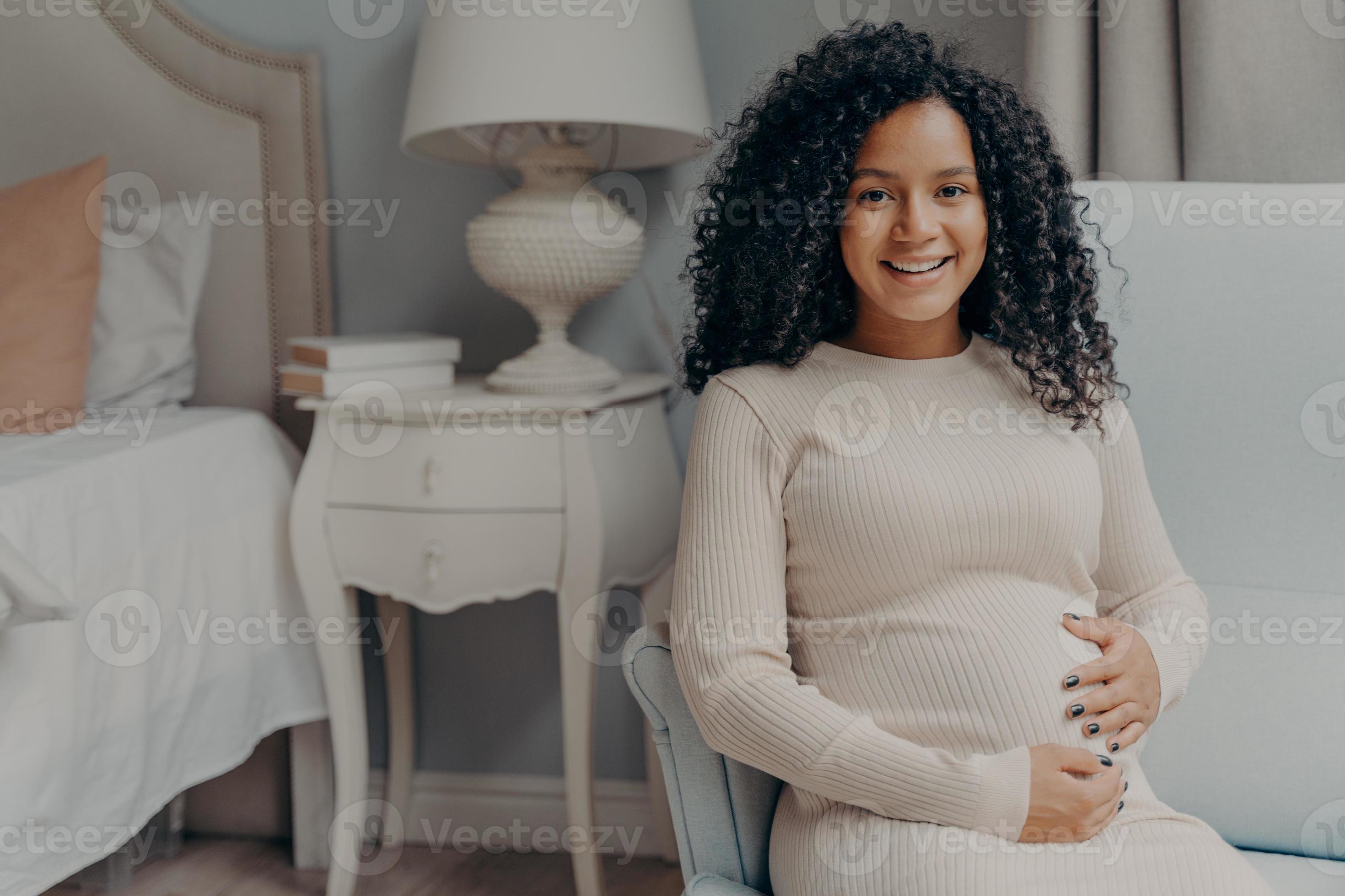 jeune femme enceinte heureuse aux cheveux bouclés tenant son ventre et  souriant à la caméra 8213349 Photo de stock chez Vecteezy