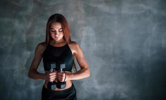 jeune femme fitness est dans la salle de gym près du mur avec des haltères  dans les mains 15239102 Photo de stock chez Vecteezy