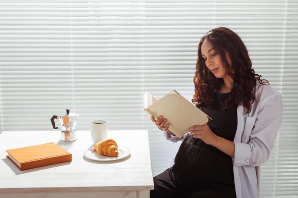 femme enceinte lit un livre pendant le petit déjeuner. concept de