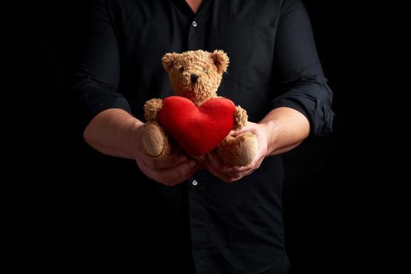 homme adulte dans une chemise noire tient un ours en peluche brun