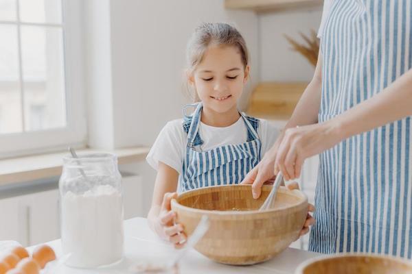 heureuse mère et fille cuisent ensemble dans la cuisine, utilisent  différents ingrédients, portent des tabliers, se tiennent contre  l'intérieur de la cuisine, la fille verse du lait à l'arc. maman  attentionnée apprend