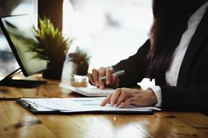 une femme d'affaires pointe pour documenter le budget et utilise une calculatrice pour examiner le bilan annuel pour calculer le budget. vérifier l'intégrité avant l'investissement. photo