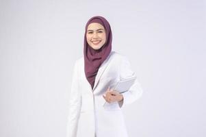 belle femme d'affaires musulmane portant un costume blanc avec hijab tenant une tablette en studio photo