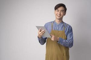 portrait de jeune homme asiatique portant un tablier tenant une tablette sur fond blanc studio, concept d'entrepreneur photo