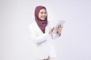 belle femme d'affaires musulmane portant un costume blanc avec hijab tenant une tablette en studio photo