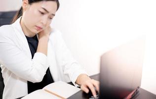 jeune asiatique se sentant douloureux du travail, assis devant l'ordinateur portable dans sa maison. concept syndrome de bureau de la femme qui travaille. photo