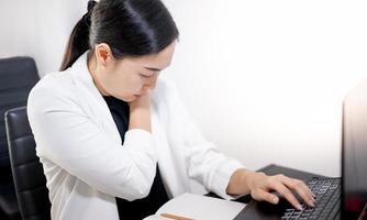 jeune asiatique se sentant douloureux du travail, assis devant l'ordinateur portable dans sa maison. concept syndrome de bureau de la femme qui travaille. photo