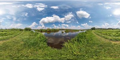 panorama hdri sphérique vue d'angle à 360 degrés sur la côte d'herbe d'un immense lac ou d'une rivière en été ensoleillé et par temps venteux avec de beaux nuages en projection équirectangulaire, contenu vr photo