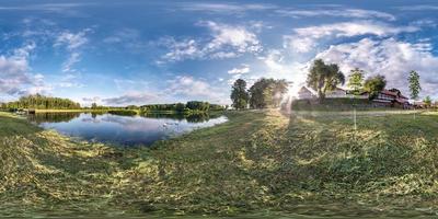panorama hdri sphérique complet et harmonieux à 360 degrés sur la côte herbeuse d'un immense lac ou d'une rivière en été avec de beaux nuages près de la maison de campagne en projection équirectangulaire, contenu vr photo
