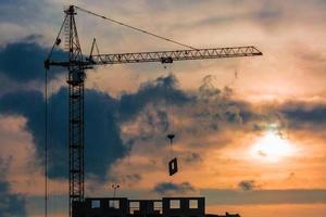 silhouette de grues à tour et de bâtiments de plusieurs étages inachevés en chantier dans les rayons du soleil couchant du beau coucher de soleil photo