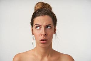 portrait d'une jeune femme séduisante portant une coiffure chignon et sans maquillage, regardant vers le haut avec un visage ennuyé, debout sur fond blanc photo