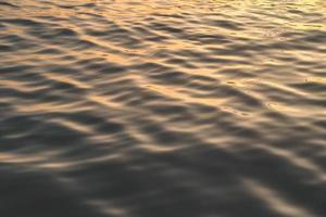 l'eau du coucher du soleil reflète les ondulations à la lumière du soleil. réflexion dorée abstraite sur le coucher du soleil sur l'eau photo