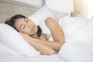 jeune femme asiatique dormant dans son lit dans la chambre. elle est allongée sur le côté et se détend les yeux fermés photo