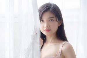 beau portrait jeune femme asiatique sexy debout la fenêtre et sourire tout en se réveillant avec la santé, corps de fille heureuse avec fraîcheur et gaie avec bien-être, mode de vie et concept de détente. photo