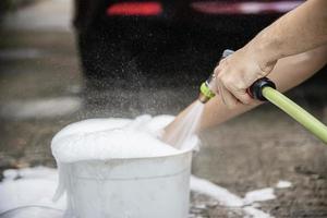 l'homme prépare de l'eau de shampoing pour laver la voiture en utilisant - les gens à la maison concept de nettoyage de voiture photo