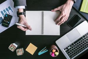 vue de dessus d'homme d'affaires écrivant des données dans un cahier sur le bureau. photo