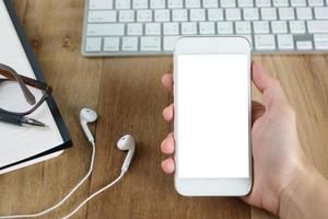 main de femme tenant l'écran vide du smartphone sur le travail de bureau en bois. photo