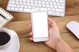 mains de femme tenant l'écran vide du smartphone sur le travail de bureau en bois. photo