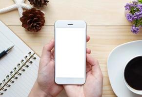 mains de femme tenant l'écran vide du smartphone sur le travail de bureau en bois. photo