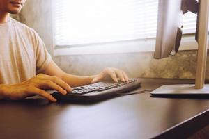 jeune homme décontracté travaillant sur ordinateur, assis au bureau, tonique avec la lumière du soleil photo