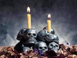 crânes avec bougie allumée et fleurs séchées sur fond sombre. photo