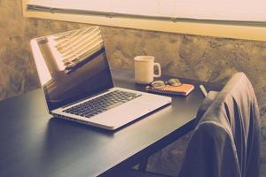 ordinateur portable avec tasse de café, cahier, lunettes et stylo sur le bureau dans la salle de bureau, ton vintage photo