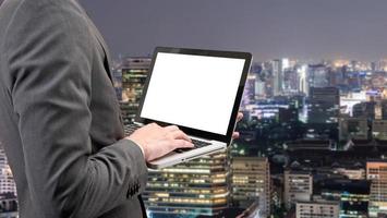 homme d'affaires détenant un ordinateur portable avec un écran blanc vierge sur fond de paysage de ville floue. photo