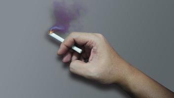 les mains tiennent la cigarette avec de la fumée sur fond de couleur isolée. photo