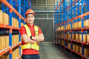 Travailleur de l'unité de fabrication réussie debout dans le centre de distribution de l'entrepôt avec les mains jointes avec casque et souriant uniforme photo