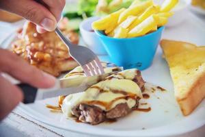 gros plan de personnes mangeant du steak avec des frites de saucisses et un plat de salade - personnes avec concept de restauration rapide photo