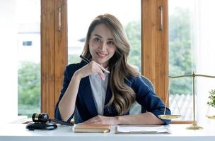 portrait, séduisante et charmante jeune femme d'affaires asiatique ou femme directrice exécutive est assise à son bureau dans un bureau moderne et lumineux. photo