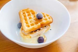 De savoureuses gaufres belges maison en forme de coeur sur un bol blanc avec des baies et du lait concentré. photo