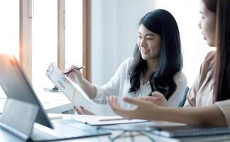 deux jeunes femmes d'affaires asiatiques discutent de la stratégie de travail et de planification du projet d'investissement. gens d'affaires parlant avec un ordinateur portable au bureau. photo